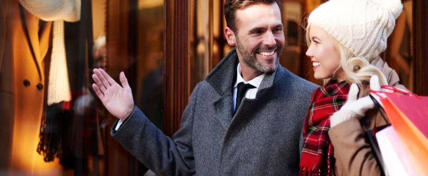 A happy couple is seen shopping around a town. They have shopping bags in their hands.