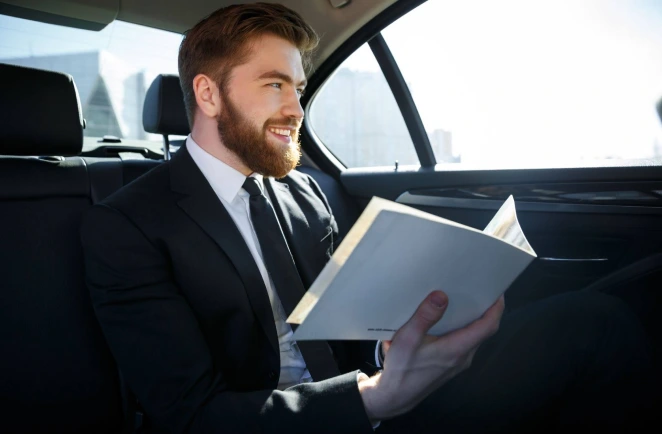An executive sitting inside a chauffeured car holding files and smiling..
