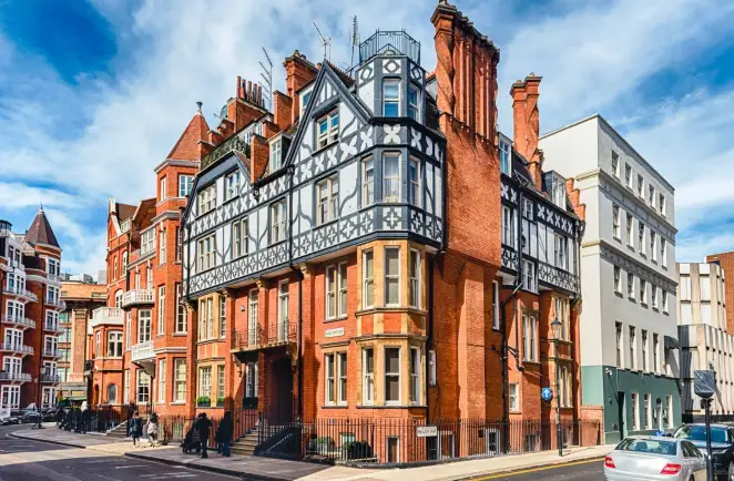 A chauffeur is waiting outside a hotel in Mayfair for the client to come. He is holding the door for the client.