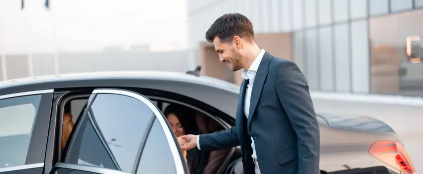 chauffeur is opening the door of the car and helping the passenger to come out.