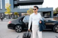 Business traveler arriving with luggage beside a premium executive sedan