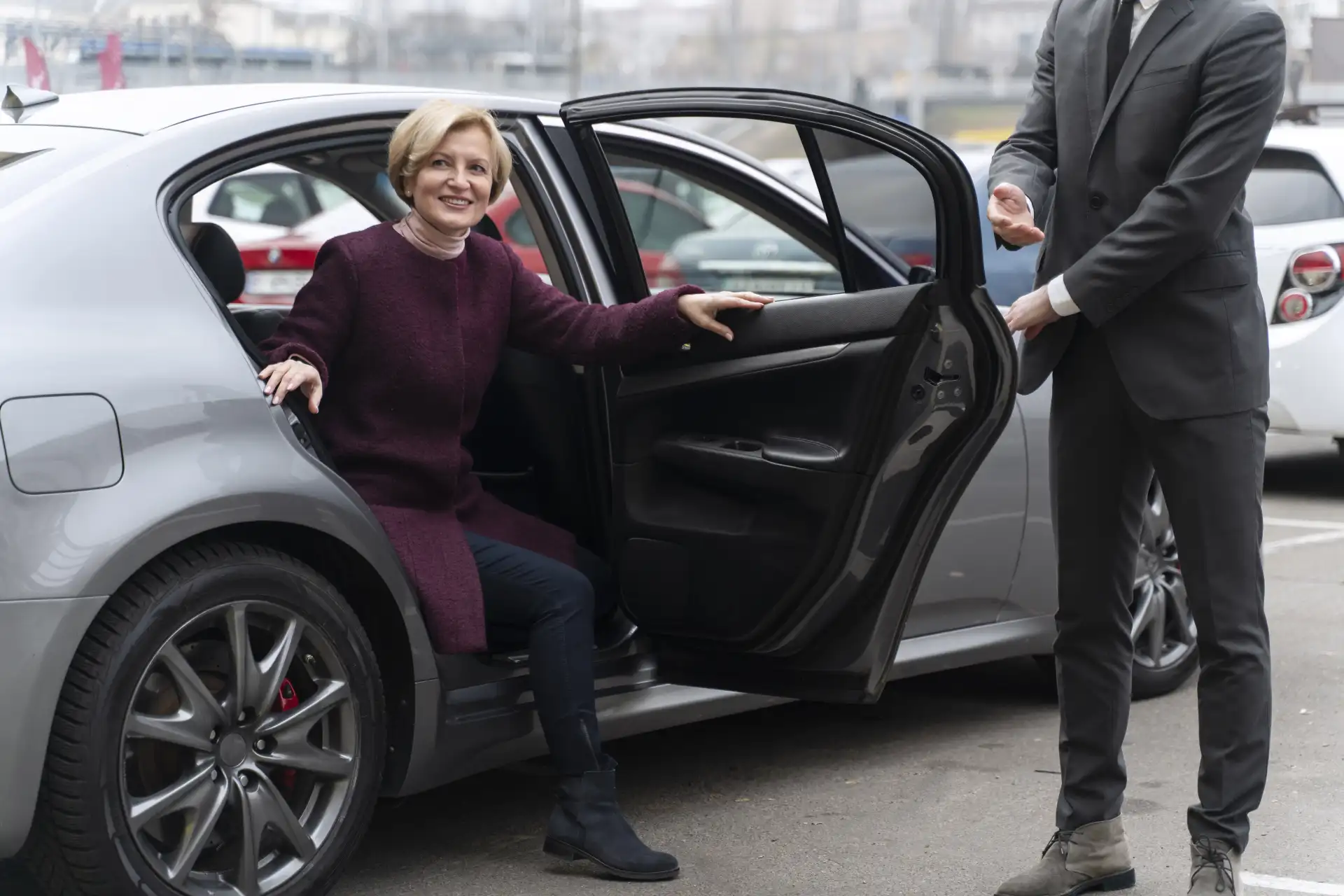 Professional chauffeur assisting an elderly passenger as she exits a luxury sedan