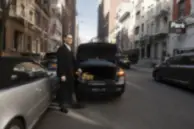 Professional chauffeur standing beside a luxury executive car outside a corporate building