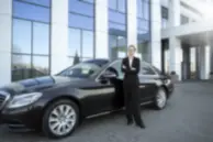 Professional chauffeur standing beside a luxury executive car outside a corporate building