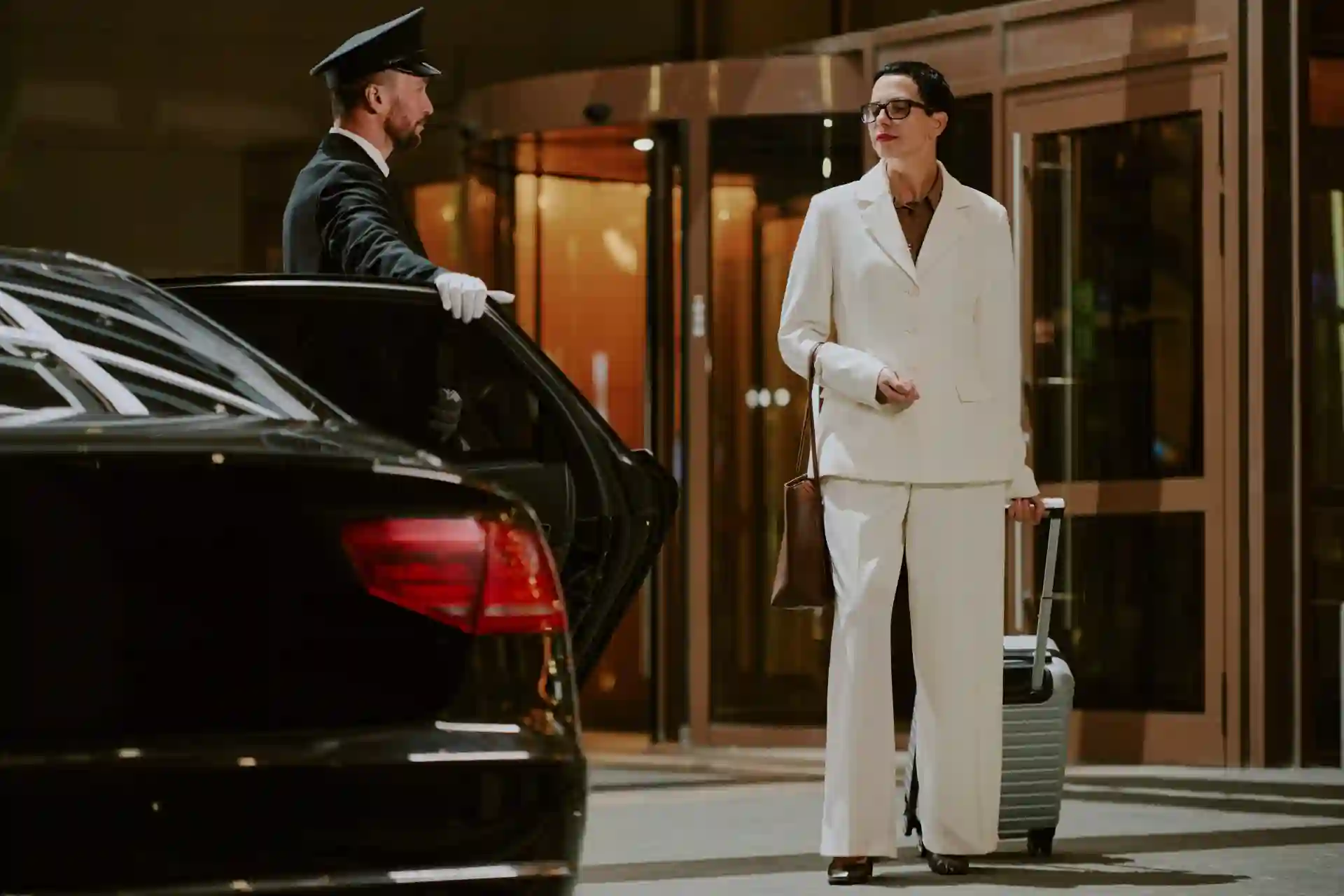 Woman arriving at a luxury hotel with a professional chauffeur opening the car door