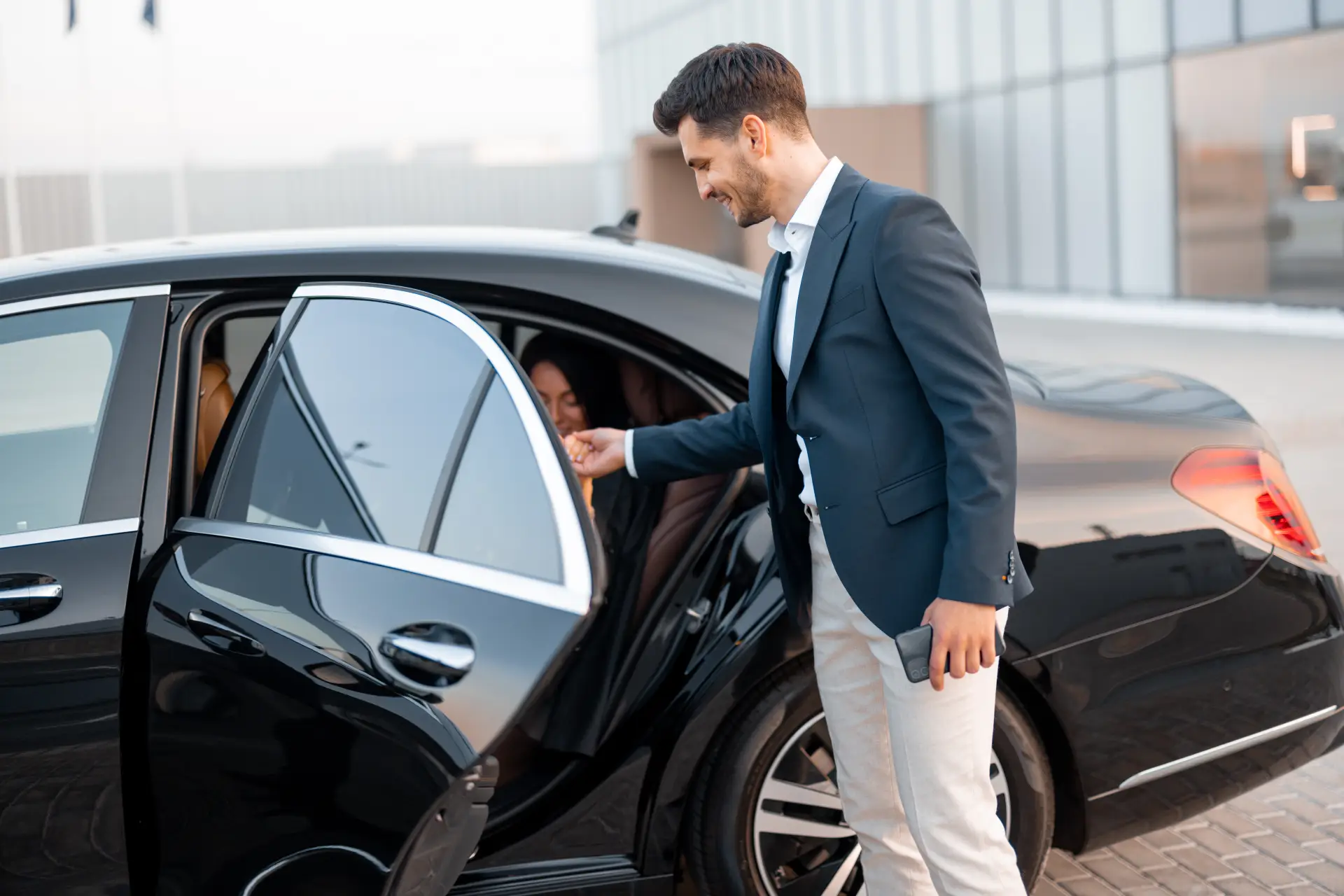 Professional chauffeur welcoming a passenger into a luxury executive car