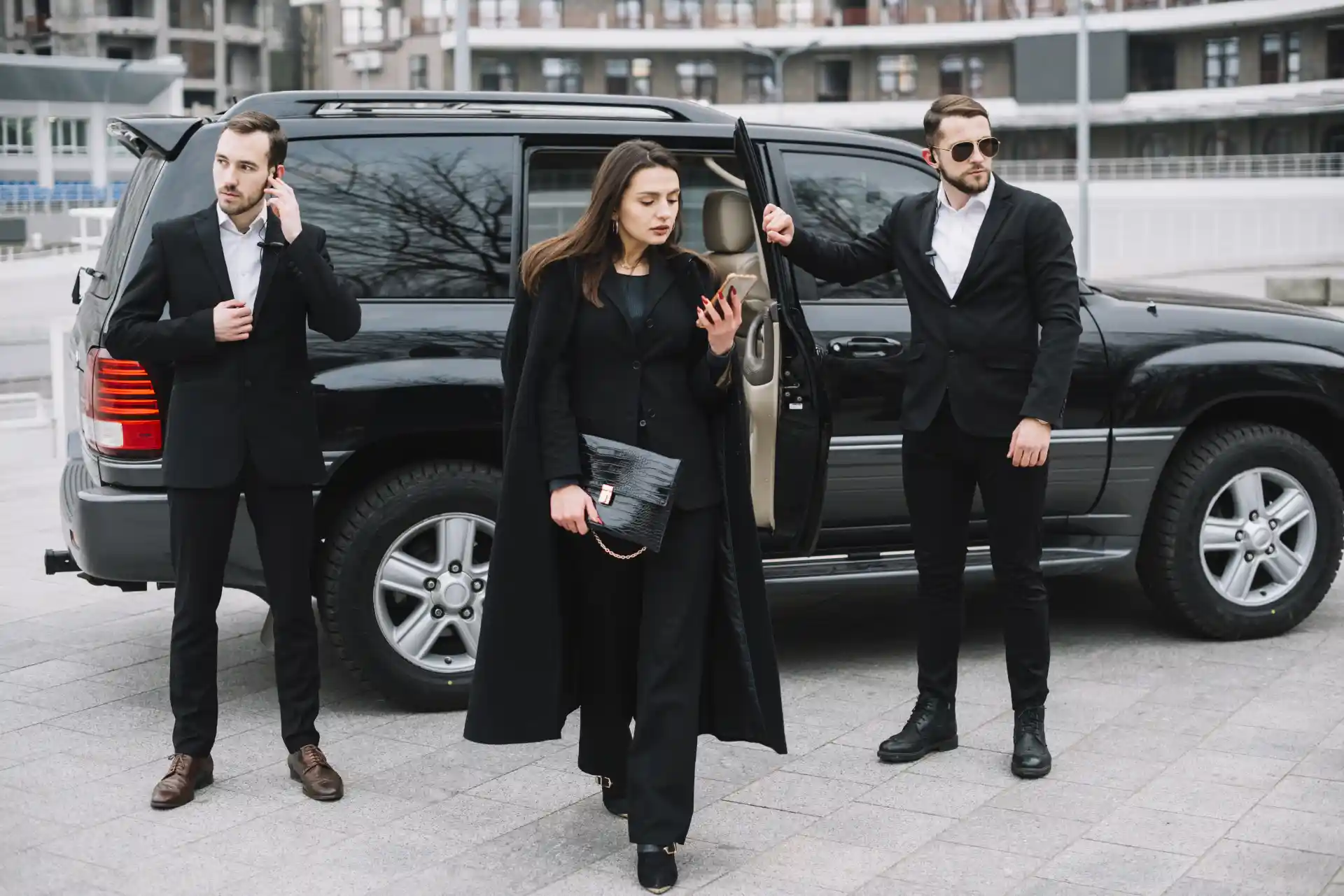 Business travelers accompanied by professional chauffeurs beside a luxury SUV during a premium transfer service