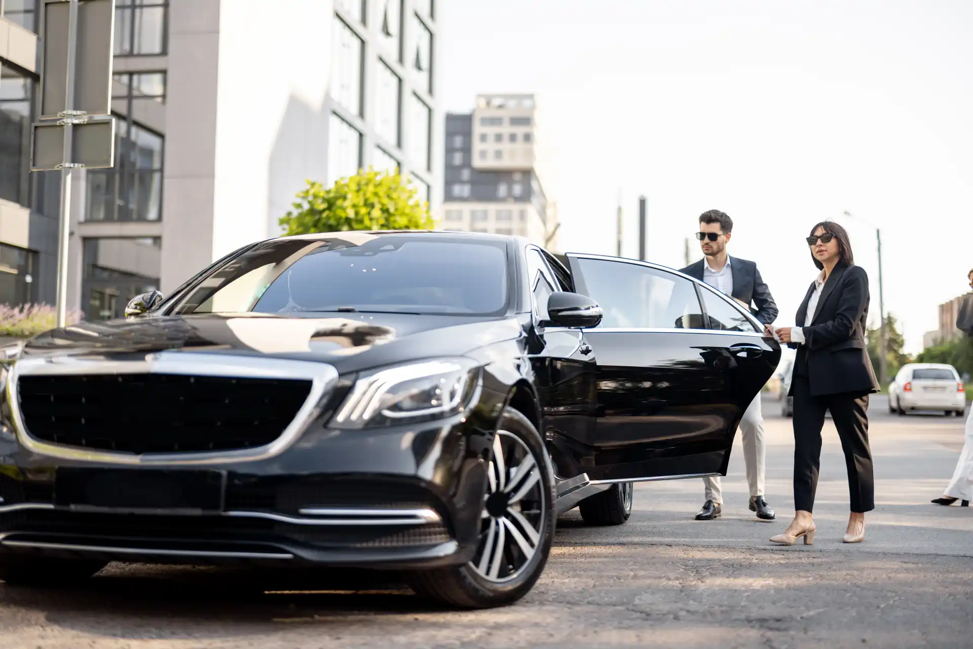 Business professionals arriving beside a luxury chauffeur-driven sedan for corporate travel