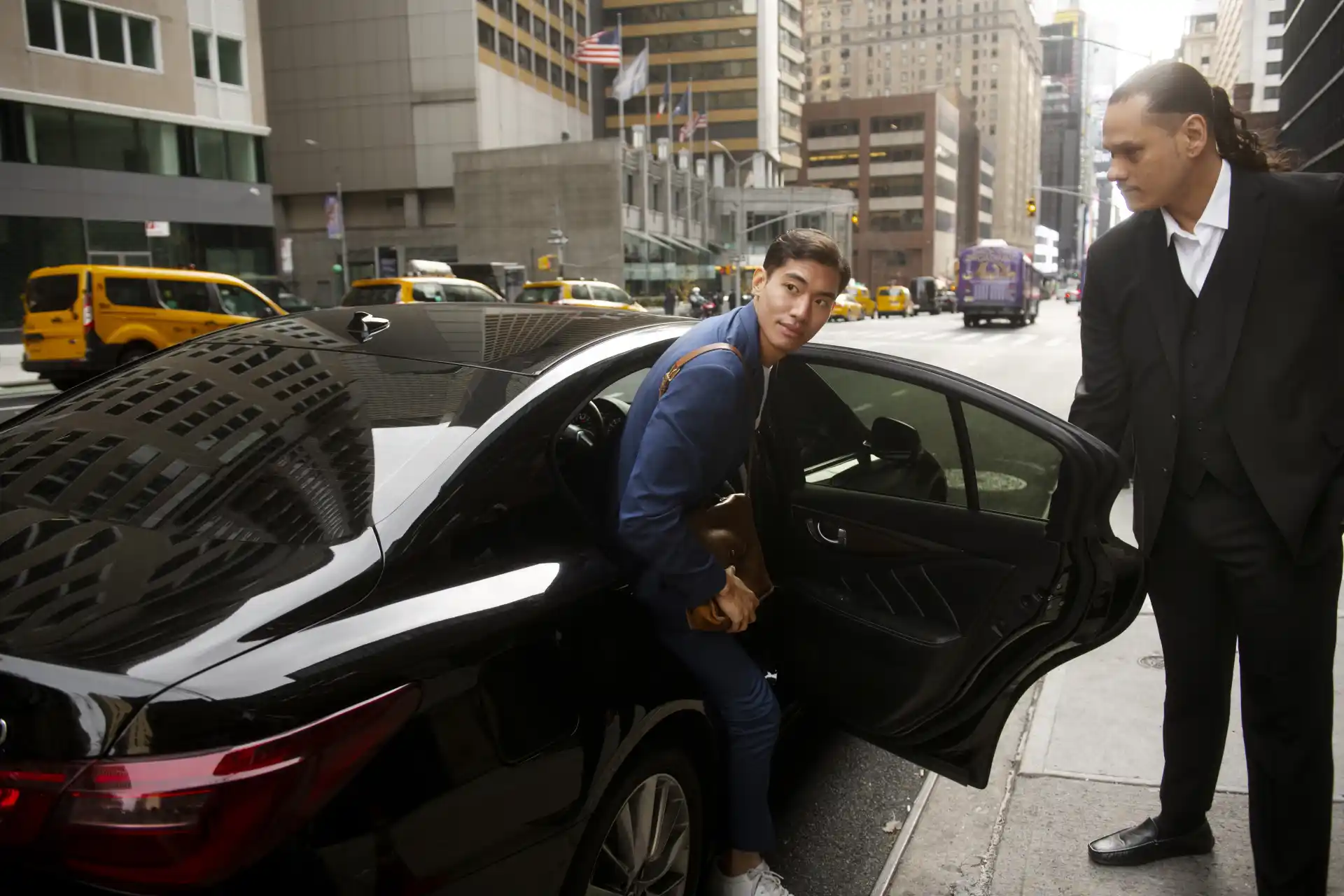 Executive chauffeur assisting a passenger during a luxury car pickup